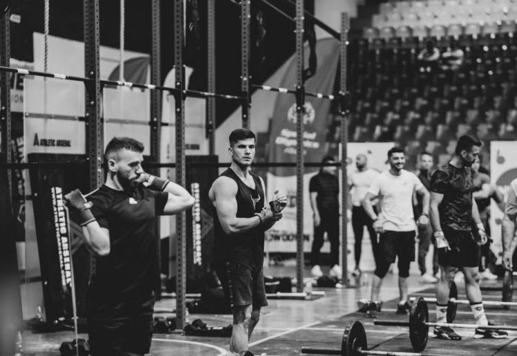 Black and white image of a fitness competition showcasing athletes and weights in a gym setting.