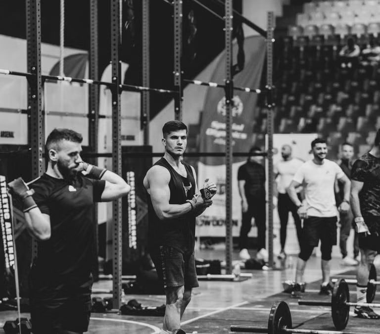 Black and white image of a fitness competition showcasing athletes and weights in a gym setting.