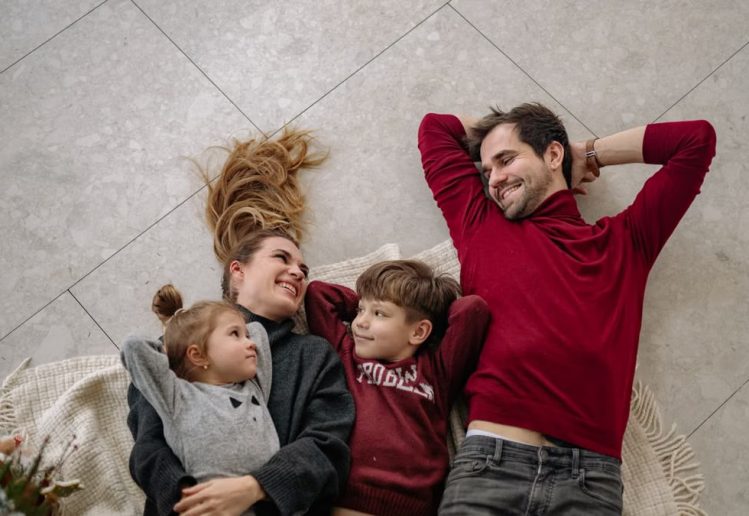 Smiling family of four lying on a blanket, sharing happiness and love indoors.
