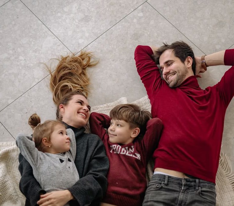 Smiling family of four lying on a blanket, sharing happiness and love indoors.